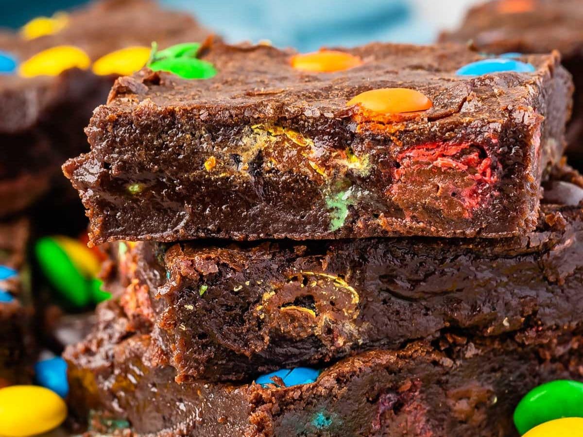 Close-up of two thick, fudgy M&M Brownies stacked, with colorful candy-coated chocolates baked inside and sprinkled on top.