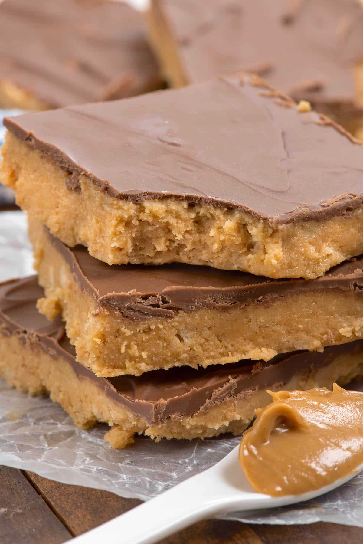 stacked peanut butter bars next to a spoonful of peanut butter.