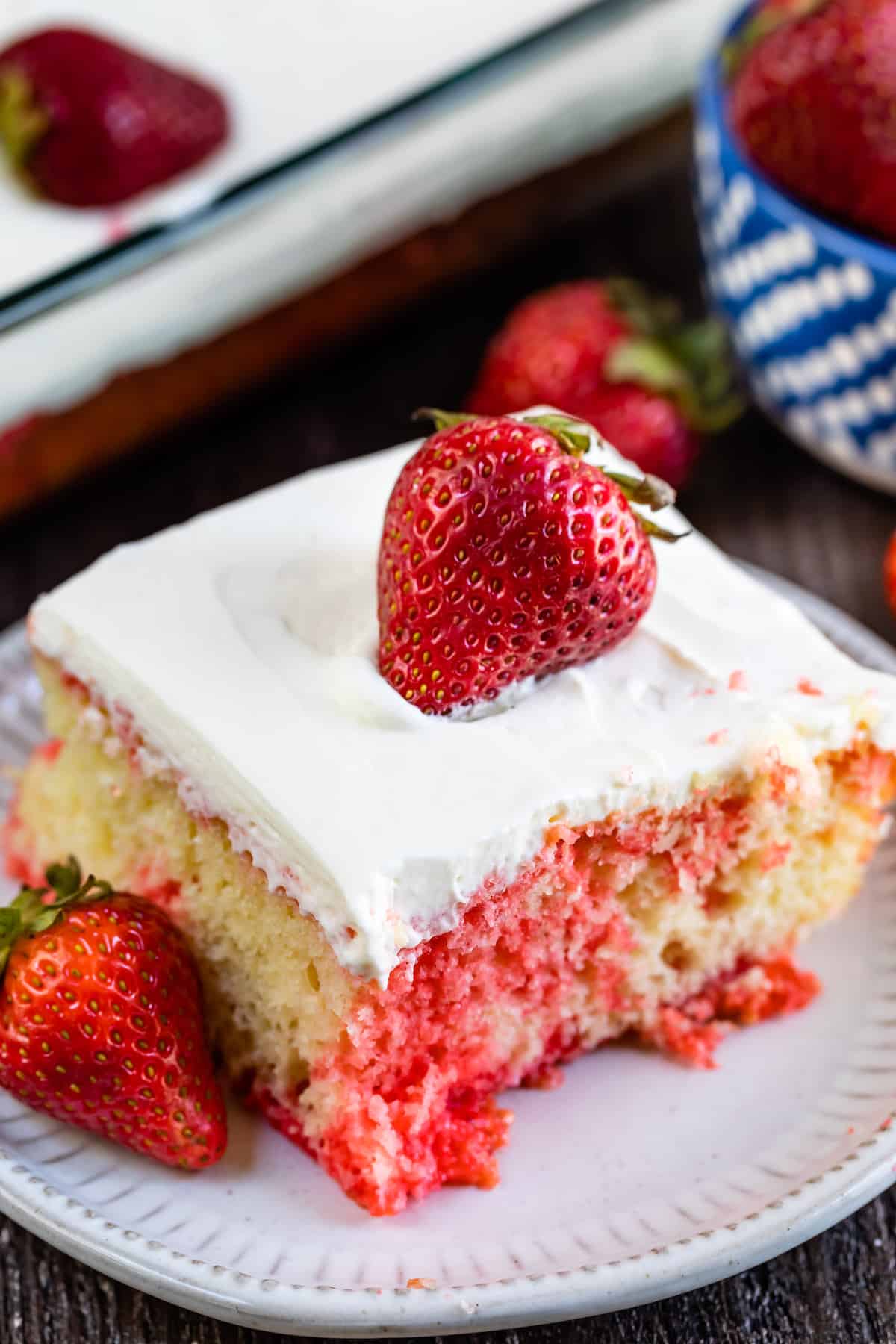 square slice of yellow cake with red dye mixed in with white frosting and a strawberry on top.