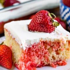 square slice of yellow cake with red dye mixed in with white frosting and a strawberry on top.