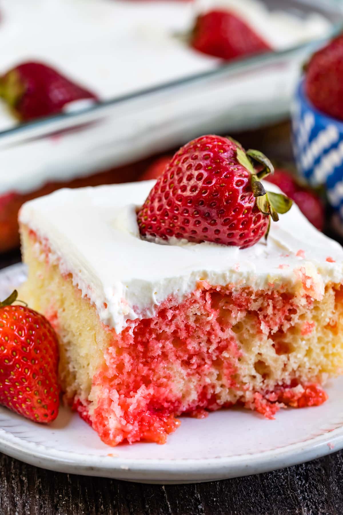 square slice of yellow cake with red dye mixed in with white frosting and a strawberry on top.