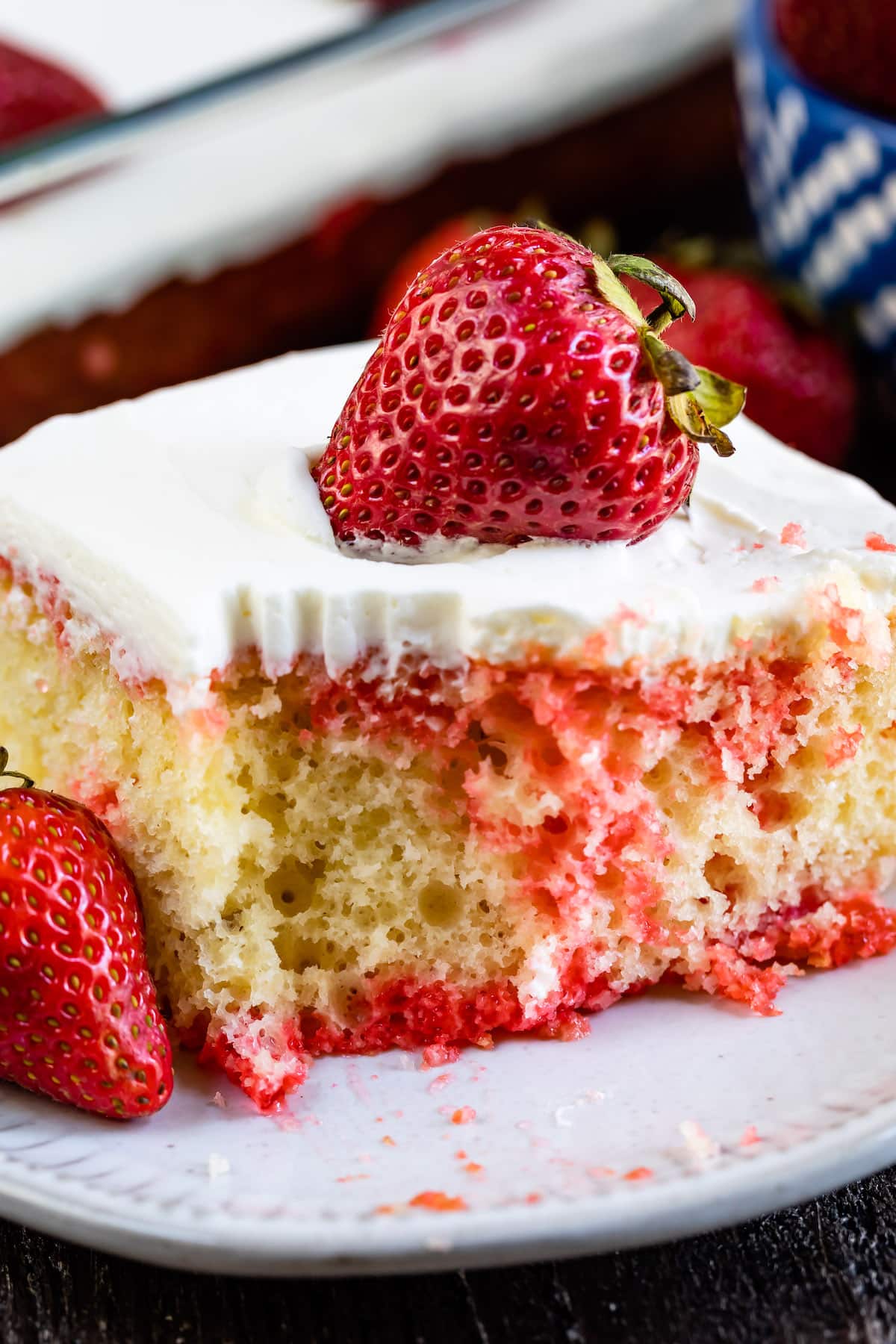 square slice of yellow cake with red dye mixed in with white frosting and a strawberry on top.