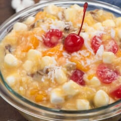 clear bowl with marshmallows and cherries and other ingredients mixed together.