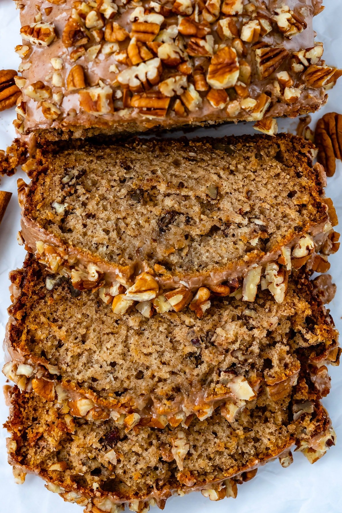 sliced banana bread topped with frosting and pecans.