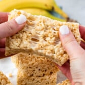 Rice Krispie Treats being torn apart with two hands and with a banana in the background.