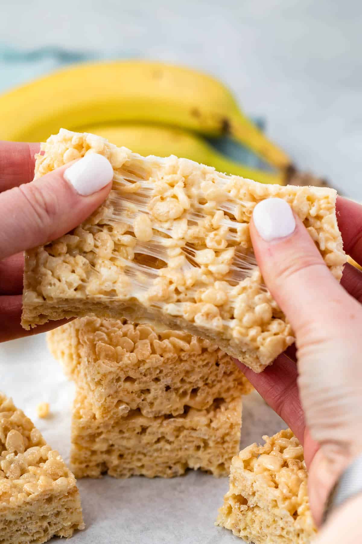 Rice Krispie Treats being torn apart with two hands and with a banana in the background.