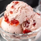 three scoops of cherry ice cream in a clear ice cream bowl with words of the image.