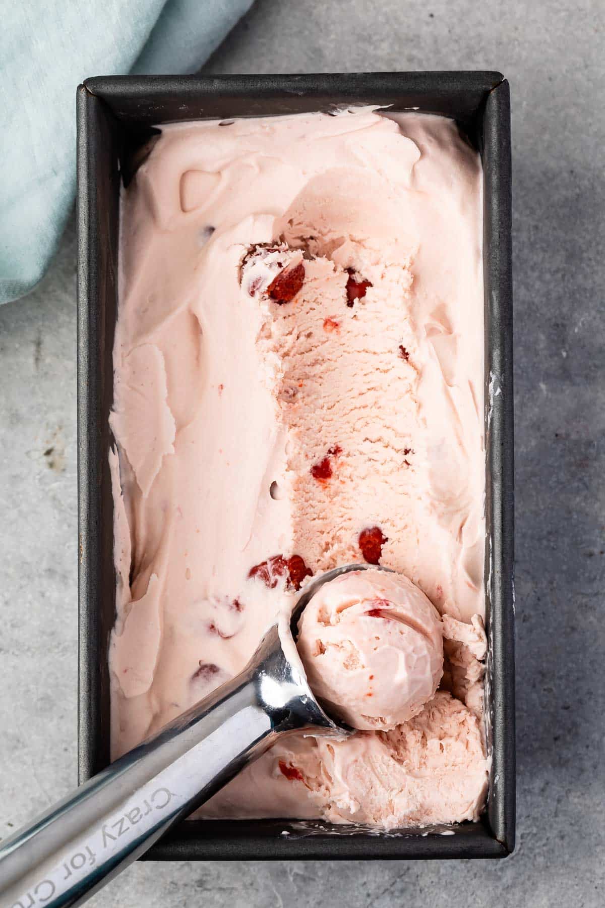 pink cherry ice cream being scooped out of a grey tin with a silver scooper.