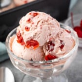 three scoops of cherry ice cream in a clear ice cream bowl.