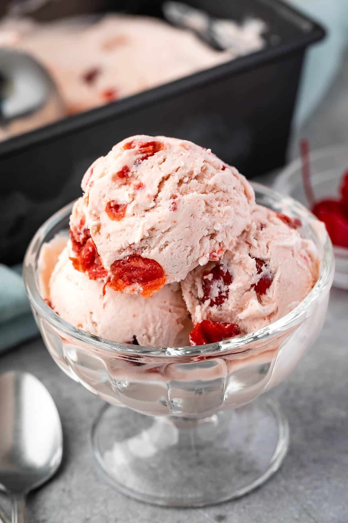 three scoops of cherry ice cream in a clear ice cream bowl.