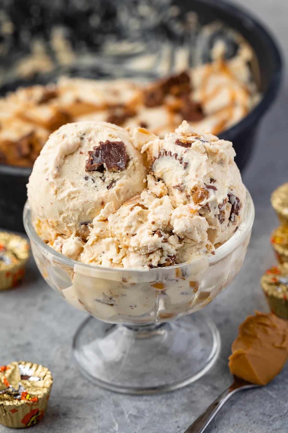 ice cream in a clear ice cream glass next to a spoonful of peanut butter.