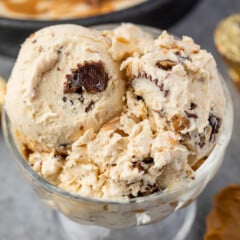 ice cream in a clear ice cream glass next to a spoonful of peanut butter.