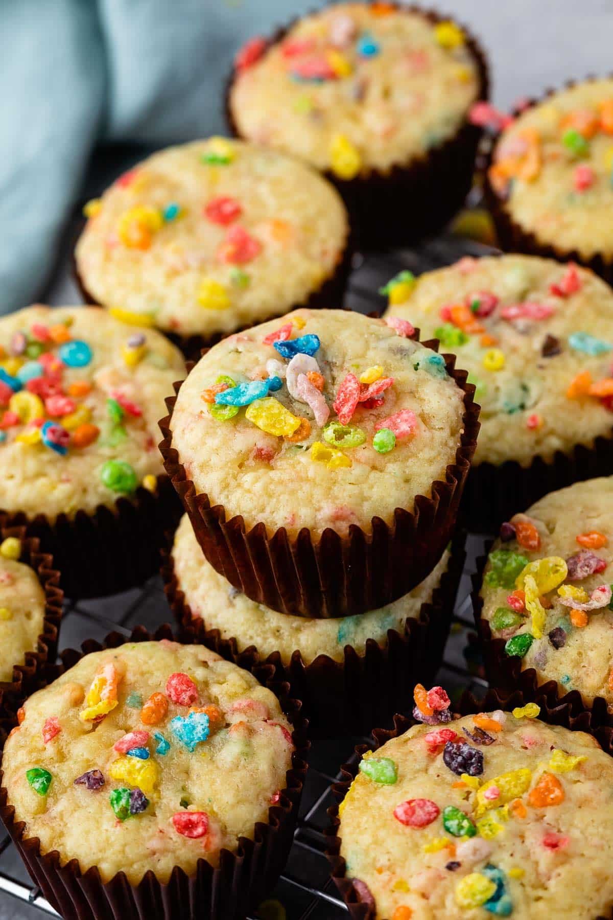 fruity pebbles muffins in a brown cupcake tin topped with fruity pebble cereal.