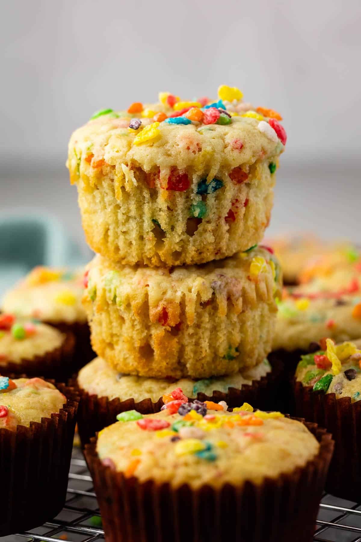 fruity pebbles muffins in a brown cupcake tin topped with fruity pebble cereal.