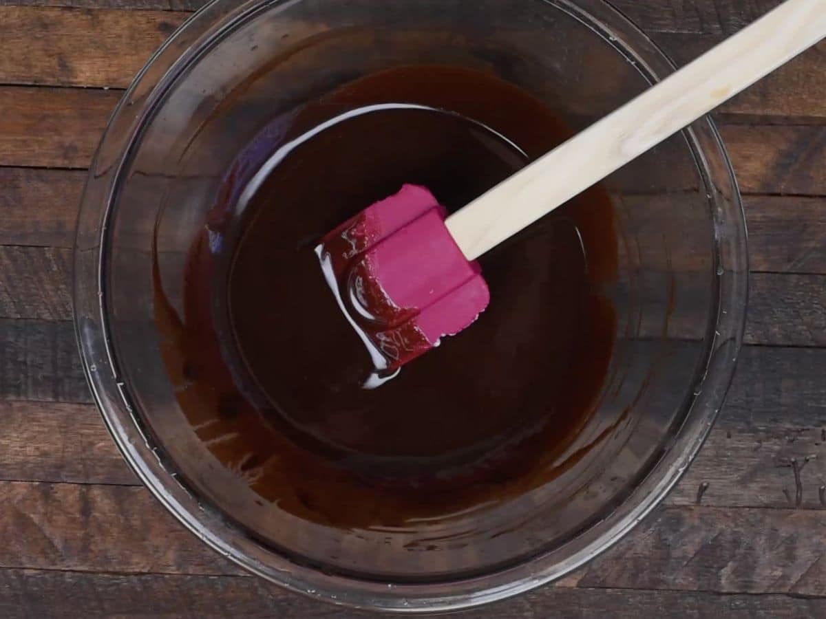 bowl of metled chocolate with pink spatula on wood background