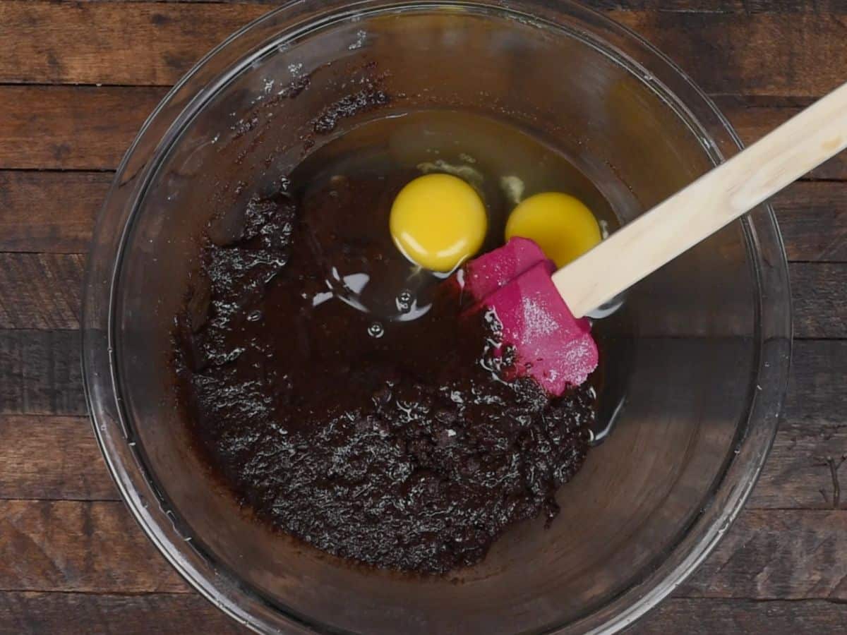 bowl of metled chocolate batter and eggs with pink spatula on wood background
