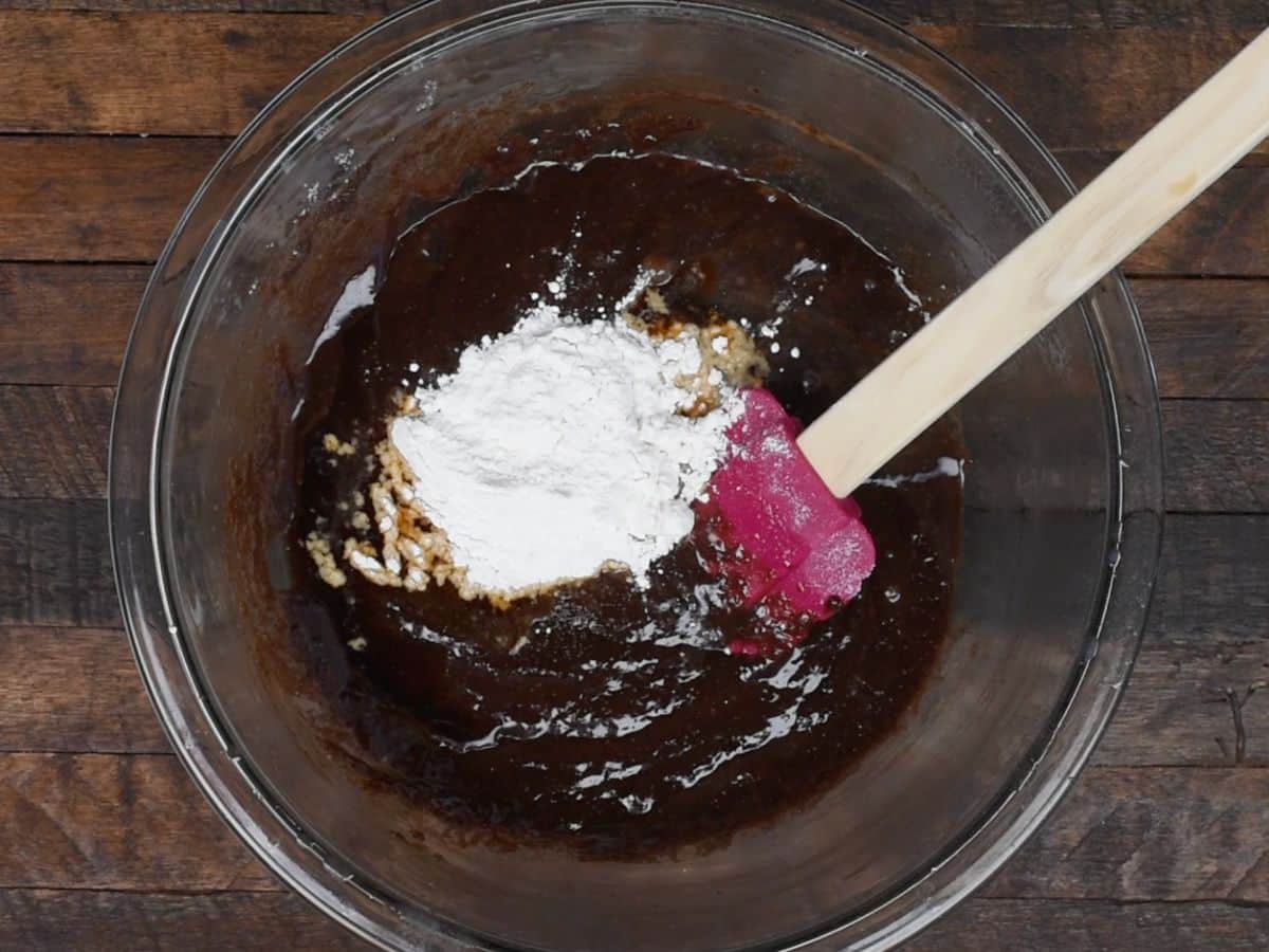 bowl of chocolate batter with flour with pink spatula on wood background