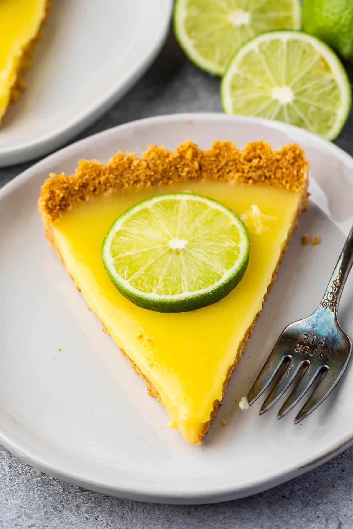 one slice of lime tart with a lime slice on top on a white plate.