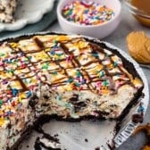 ice cream pie in a pie tin topped with chocolate and caramel sauce and sprinkles.