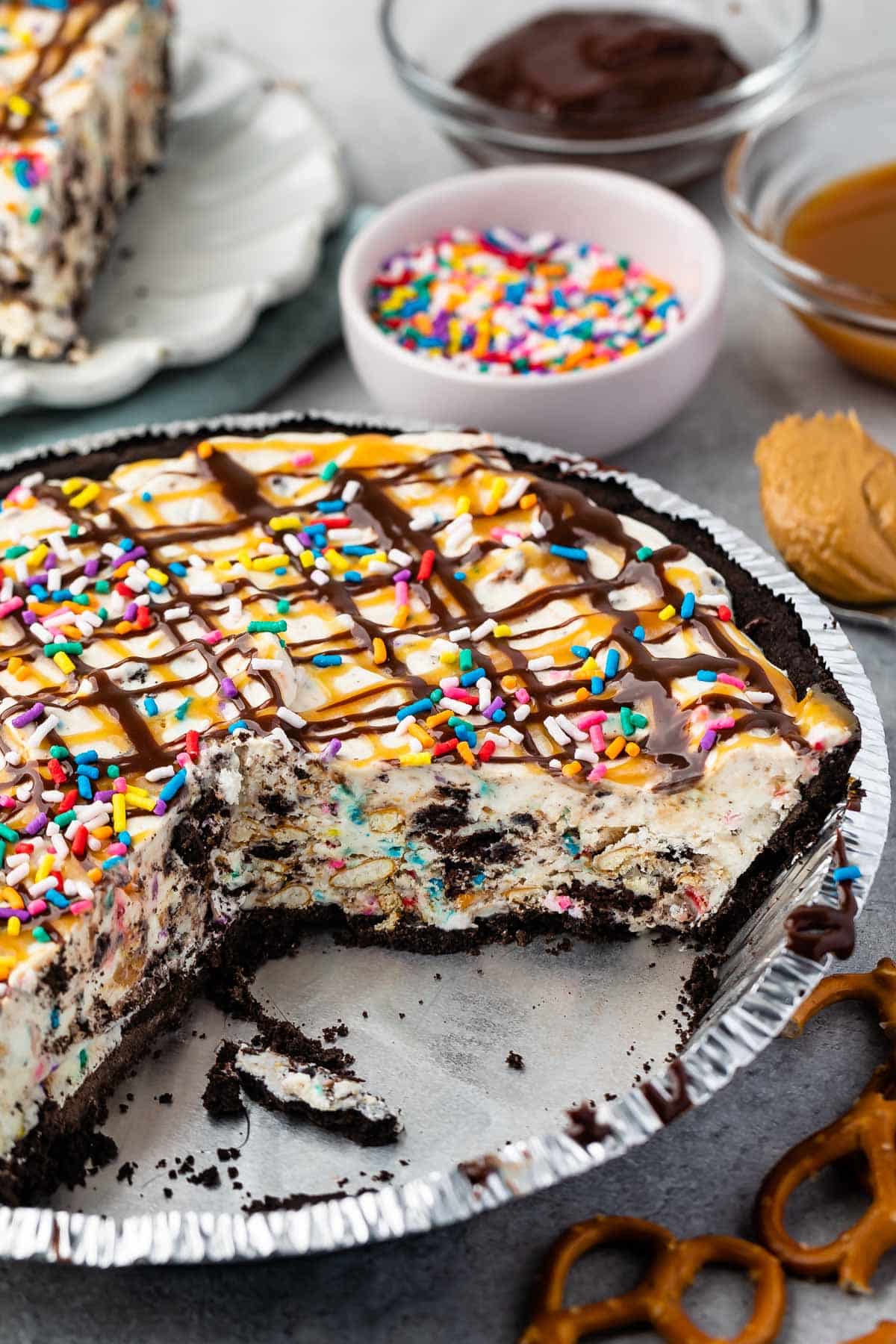 ice cream pie in a pie tin topped with chocolate and caramel sauce and sprinkles.