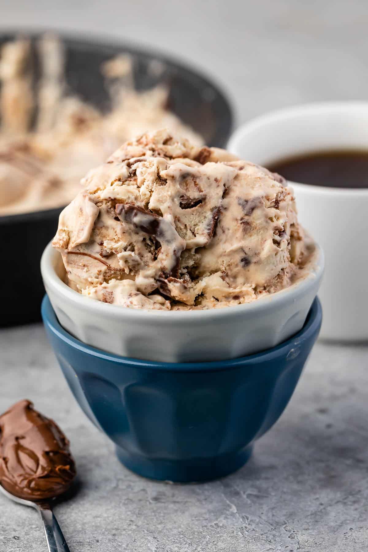 ice cream in a white and blue cup next to a spoonful of nutella.