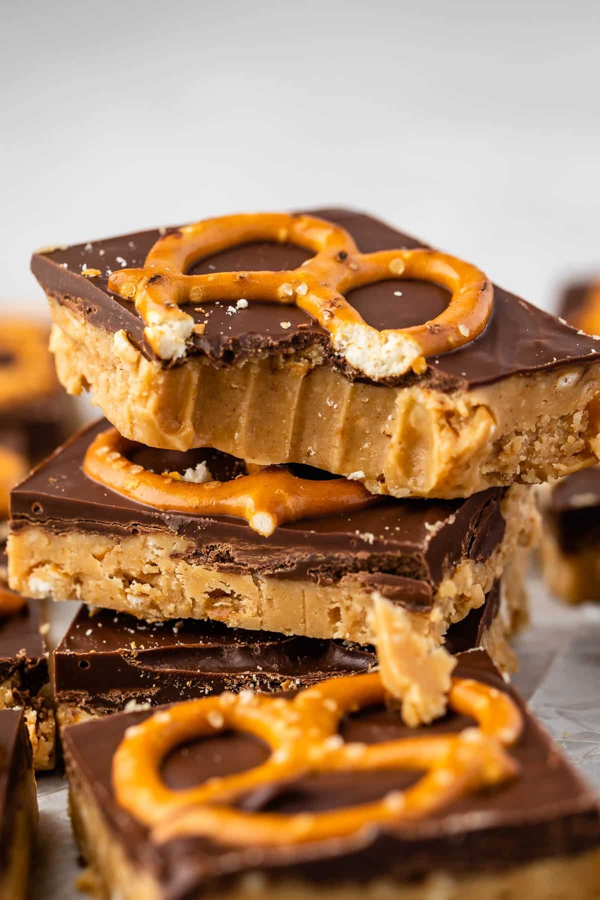 stacked peanut butter bars with a layer of chocolate on top with a pretzel.