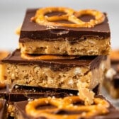stacked peanut butter bars with a layer of chocolate on top with a pretzel.