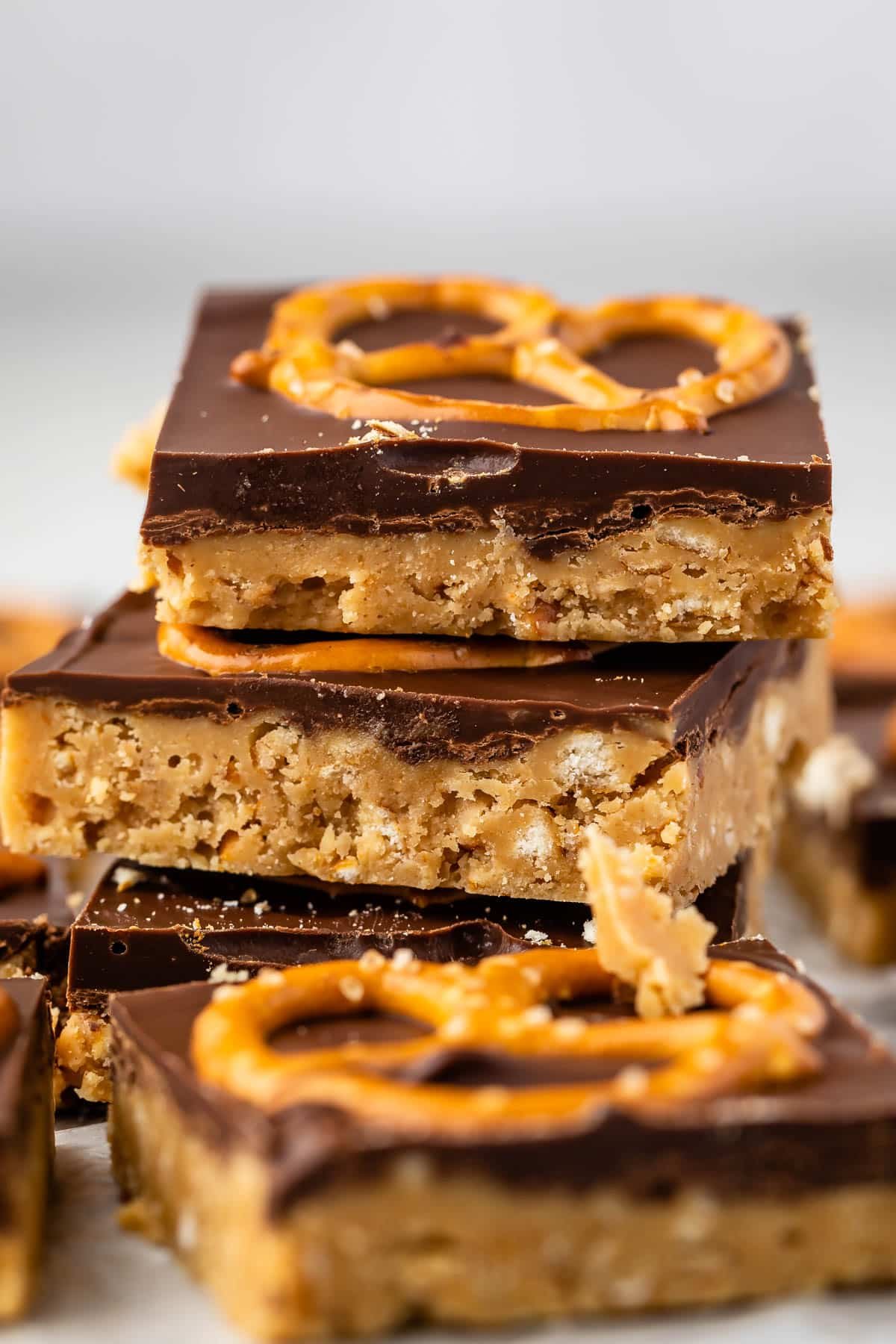 stacked peanut butter bars with a layer of chocolate on top with a pretzel.