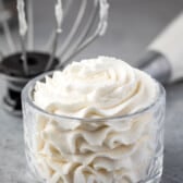 whipped cream in glass bowl with whisk attachment and pastry bag behind.