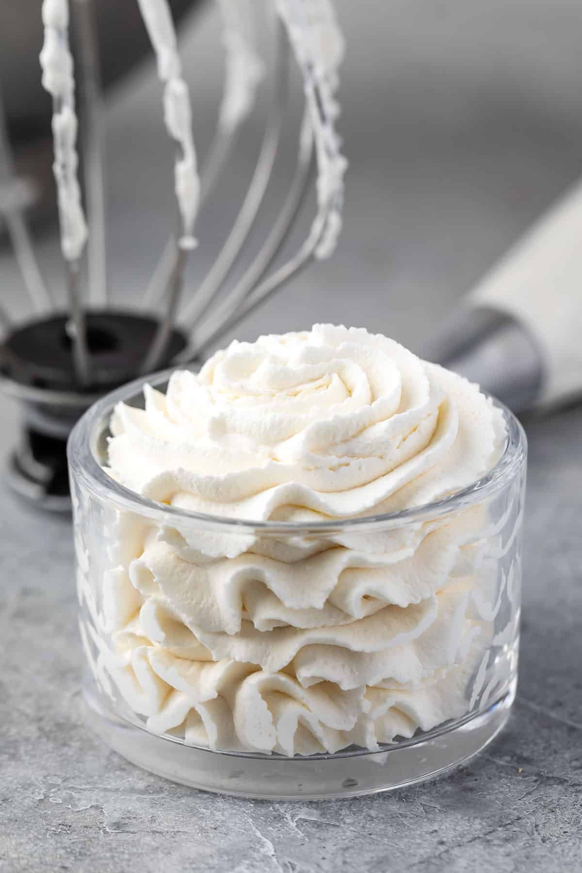 whipped cream in glass bowl with whisk attachment and pastry bag behind.