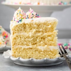 slice of 3 layer yellow cake with vanilla frosting on white plate with fork.