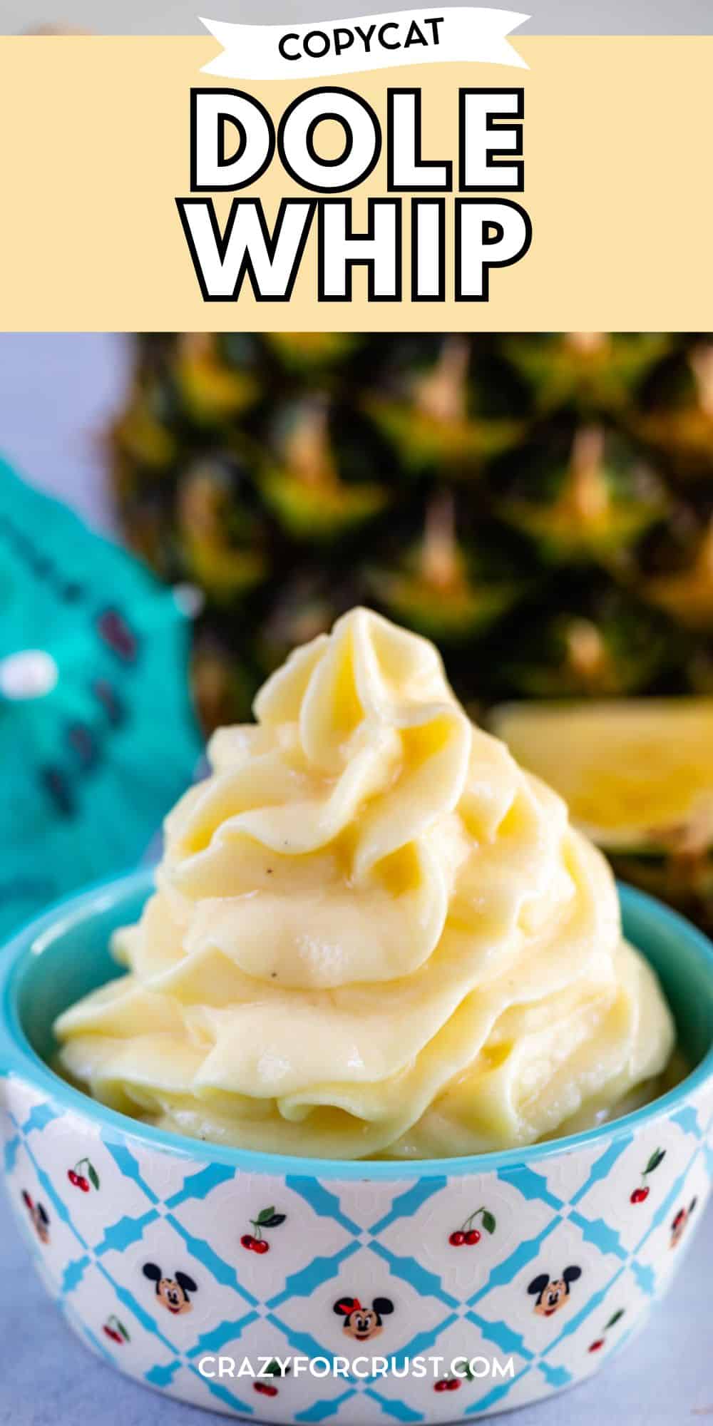 A bowl of creamy, yellow Dole Whip soft serve sits in a blue patterned bowl, with a pineapple and a teal napkin in the background. The image has text that reads Copycat Dole Whip at the top, perfect for showcasing your favorite dole whip recipe.