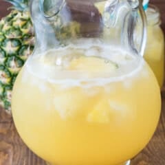yellow party punch in a clear glass with pineapple in the back.