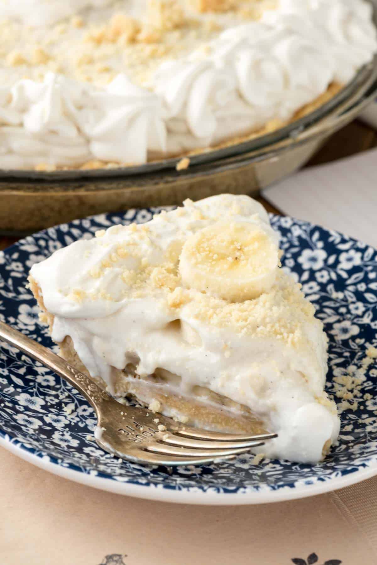 pie topped with a banana slice on a blue and white plate next to a fork.