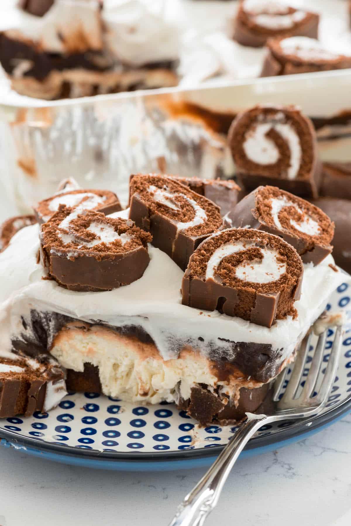 Swiss roll dessert on a plate next to a fork with sliced Swiss rolls on top.