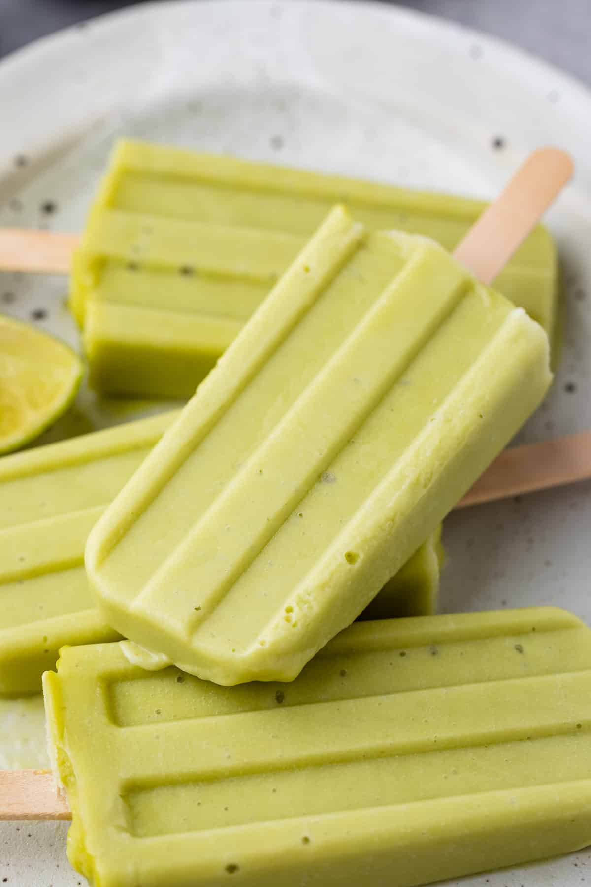 stacked green popsicles with wooden sticks at the bottoms on a white plate