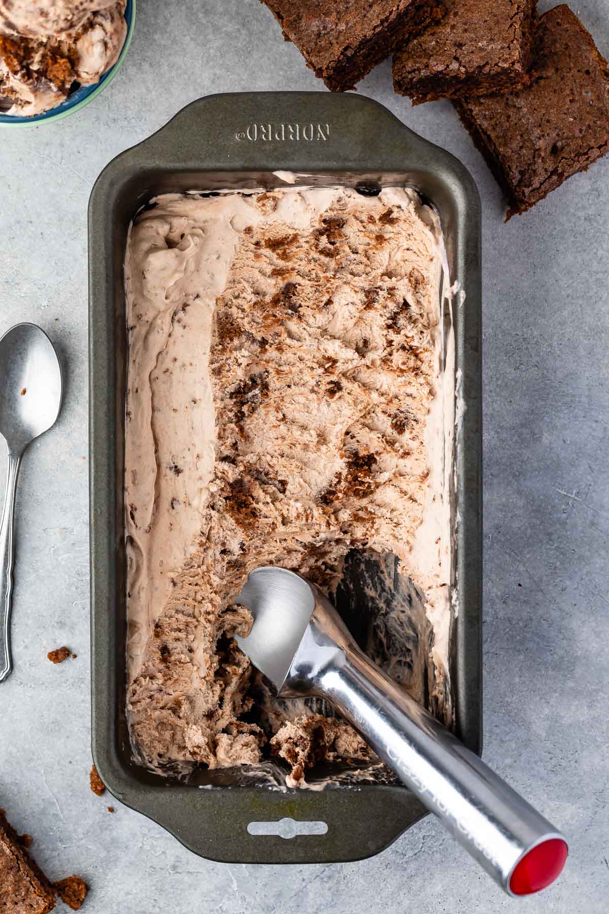 brownie batter ice cream in a grey ice cream tin with a silver ice cream scooper.