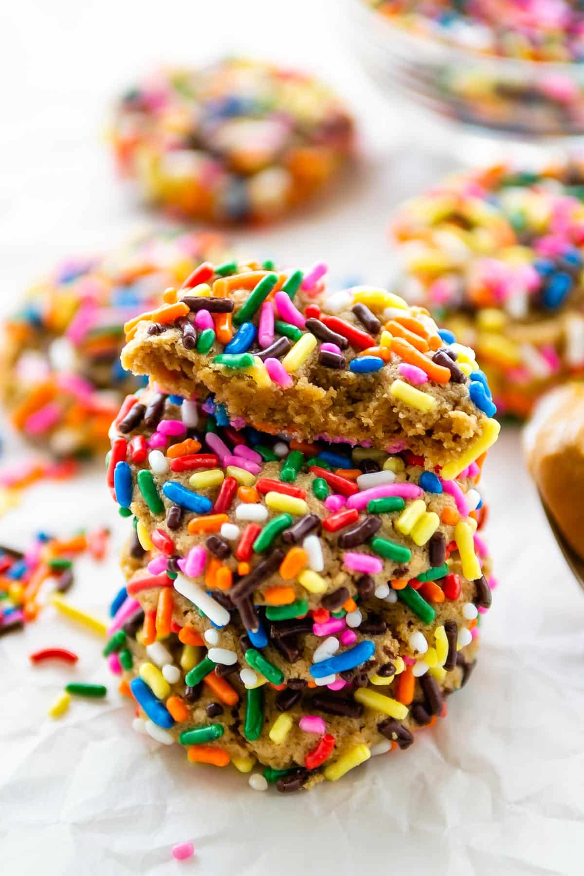 stack of 4 cookies coated in rainbow sprinkles with one cut in half on top.