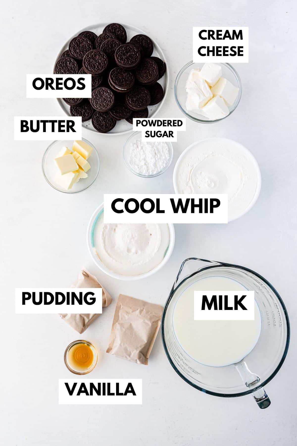 Top-down view of labeled chocolate lasagna dessert ingredients in bowls: Oreos, cream cheese, butter, powdered sugar, Cool Whip, vanilla, milk, and pudding mix packets arranged on a white surface.