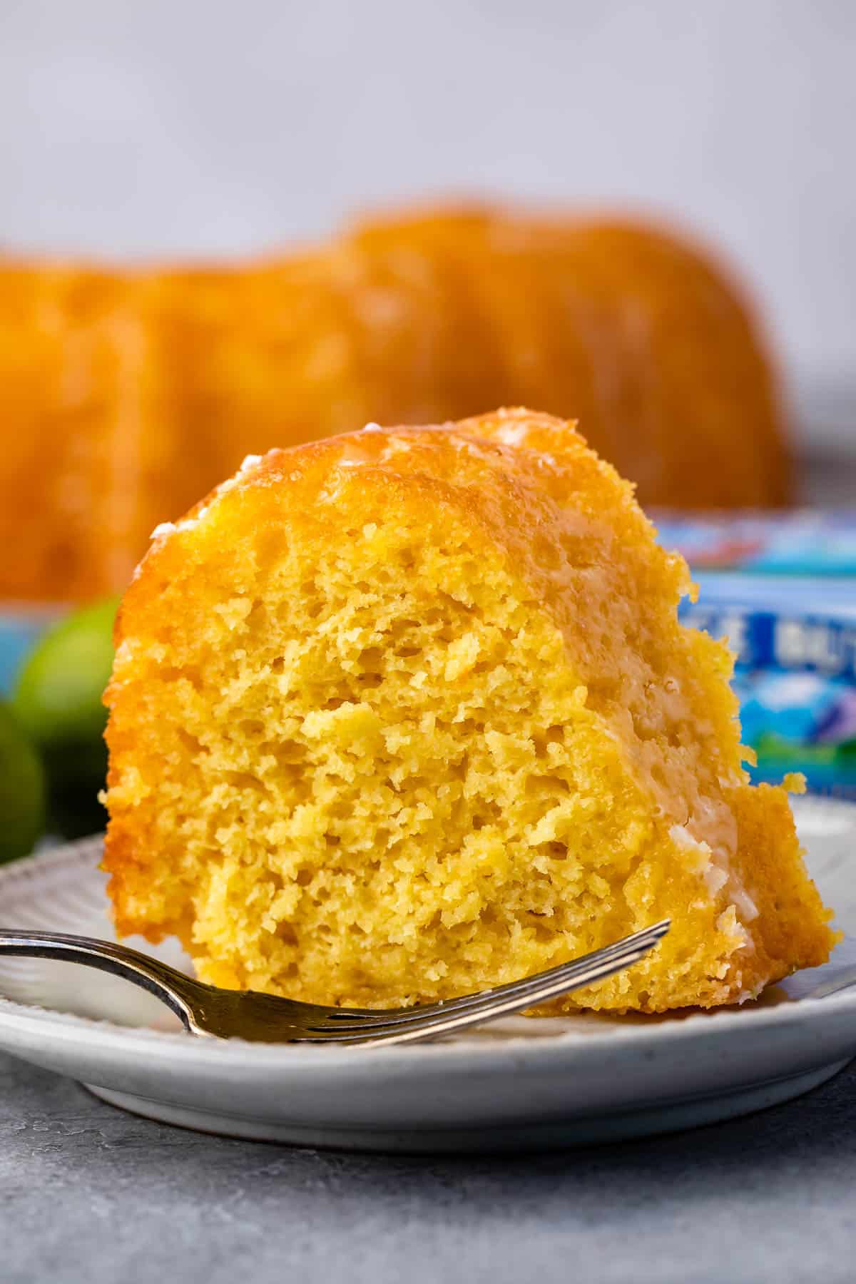 slicer of cake on white plate with fork and limes behind and butter box.