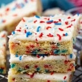 stacked sugar cookie bars with vanilla frosting and red white and blue sprinkles on top.