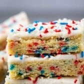 stacked sugar cookie bars with vanilla frosting and red white and blue sprinkles on top.