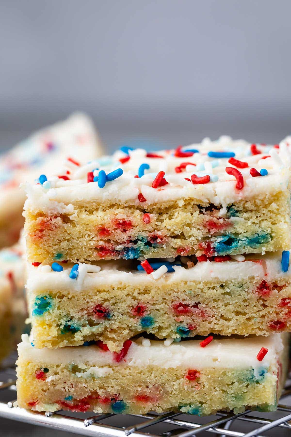 stacked sugar cookie bars with vanilla frosting and red white and blue sprinkles on top.