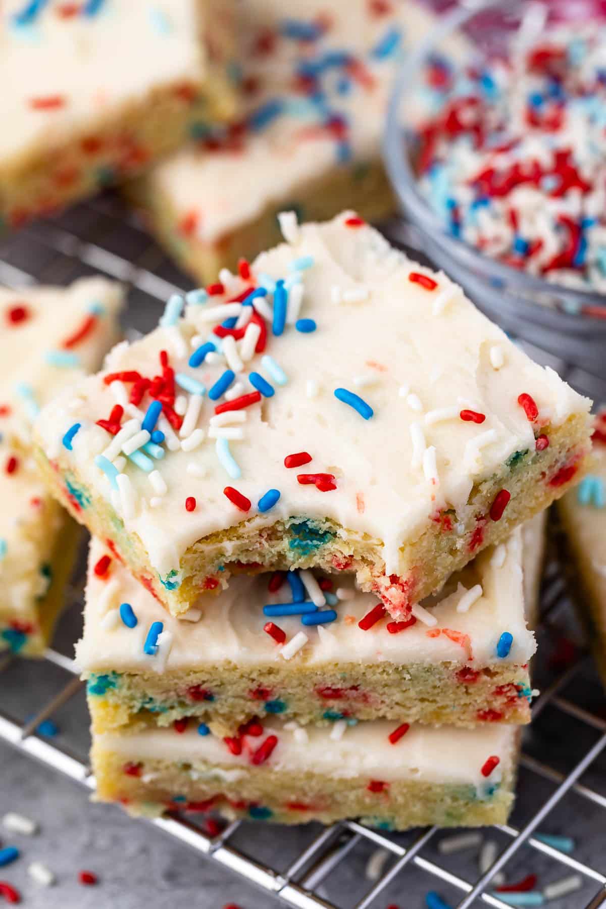 stacked sugar cookie bars with vanilla frosting and red white and blue sprinkles on top.