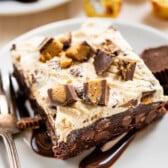 square slice of ice cream brownies on a white plate next to a fork.