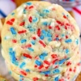 A stack of 4th of July Cookies topped with red, white, and blue sprinkles, with a blurred background featuring stripes in matching colors.