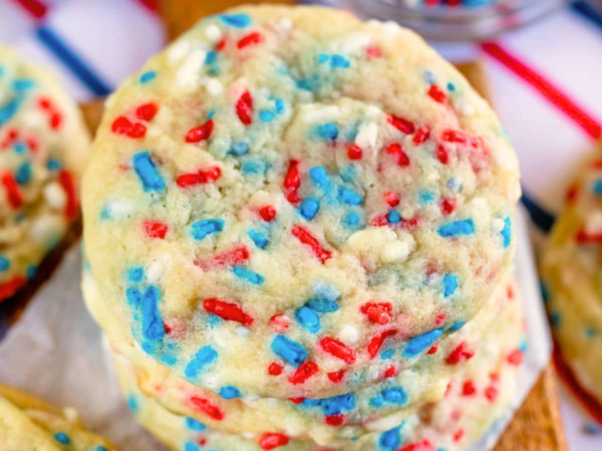 A stack of 4th of July Cookies topped with red, white, and blue sprinkles, with a blurred background featuring stripes in matching colors.