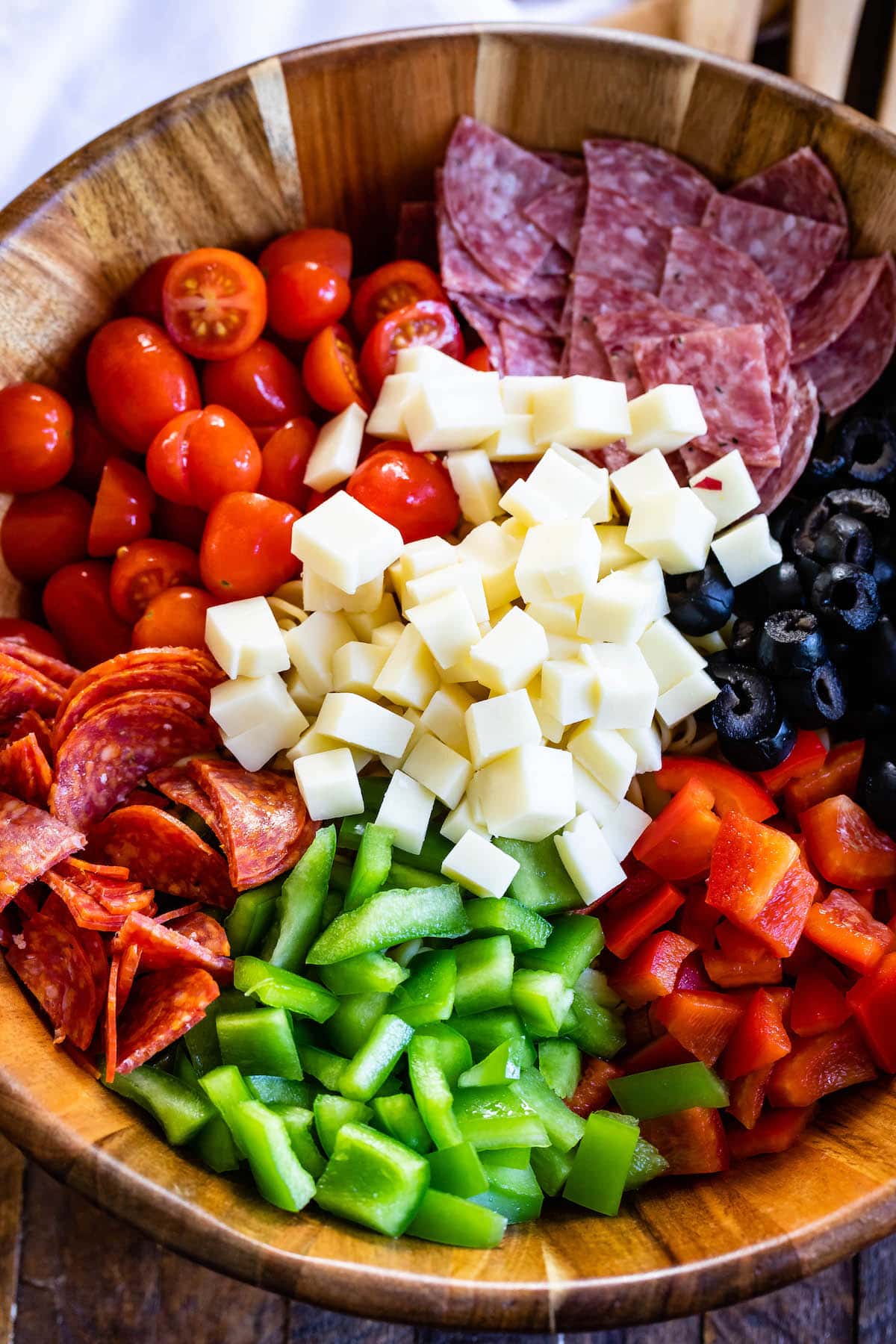 pasta and salami and other mix ins together in a wooden bowl.