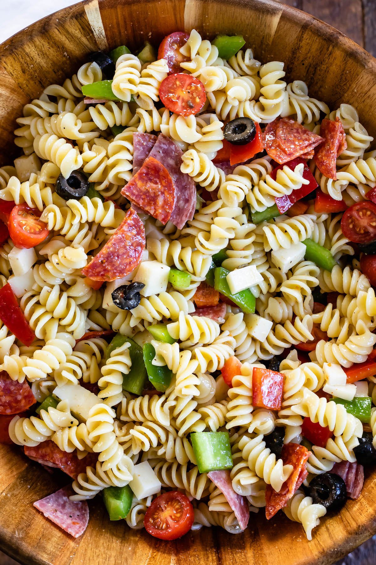 pasta and salami and other mix ins together in a wooden bowl.