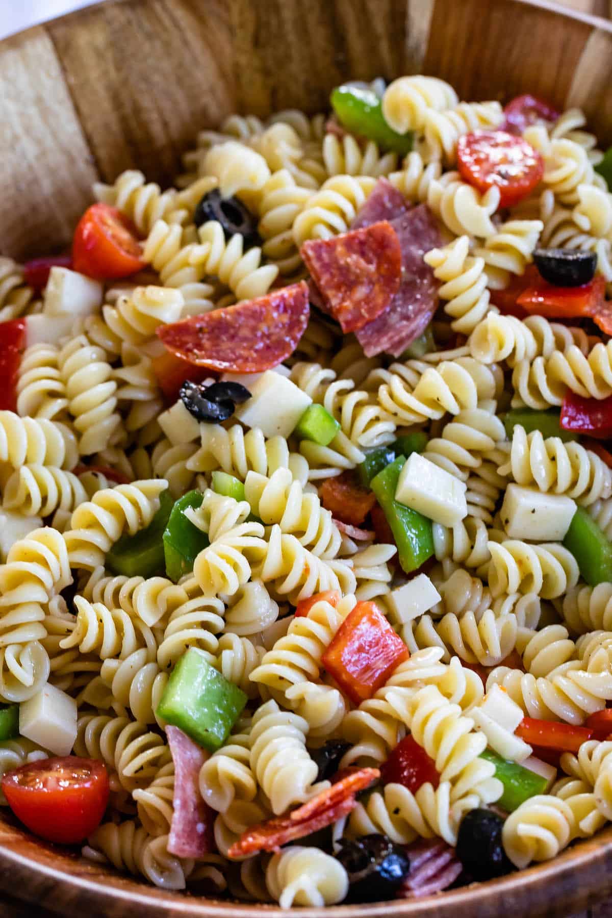 pasta and salami and other mix ins together in a wooden bowl.